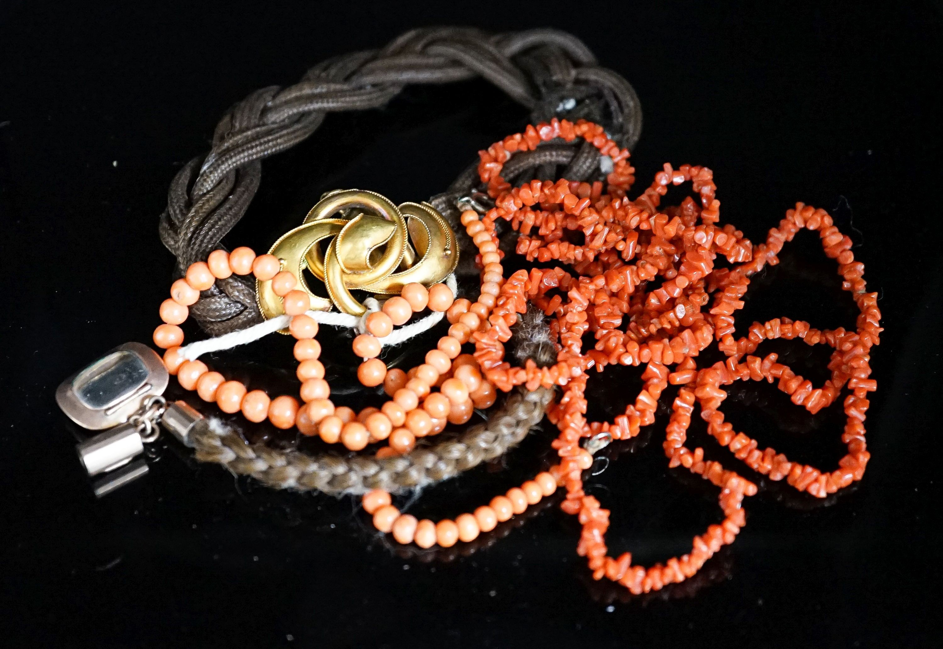 A Victorian yellow metal mounted hairwork bracelet, hung with plaited hair tassel with yellow metal fob, and two coral necklaces.